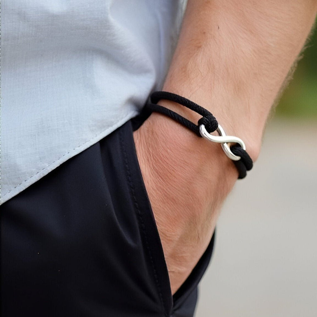 Bracelet cordon noir avec ornement infini en métal argenté, ajustable au poignet.