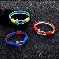 Trois bracelets cordon multicolores avec manilles en acier inoxydable sur fond noir texturé.