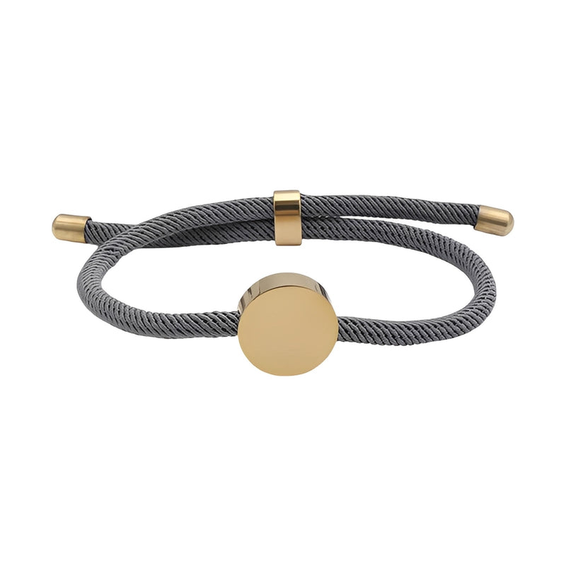 Bracelet cordon gris avec médaillon rond en acier inoxydable doré, finition brillante, fermeture coulissante dorée.
