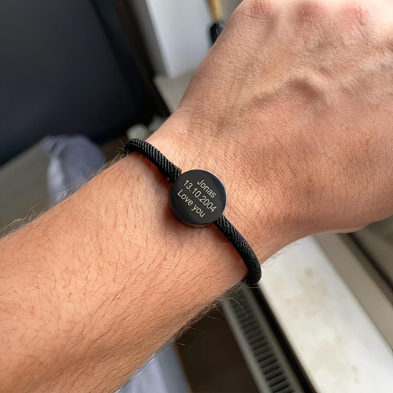 Bracelet cordon noir avec médaillon rond en acier inoxydable gravé d’un prénom et d’une date.