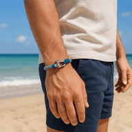 Bracelet cordon bleu et blanc avec mousqueton en métal, style marin, porté à la plage.