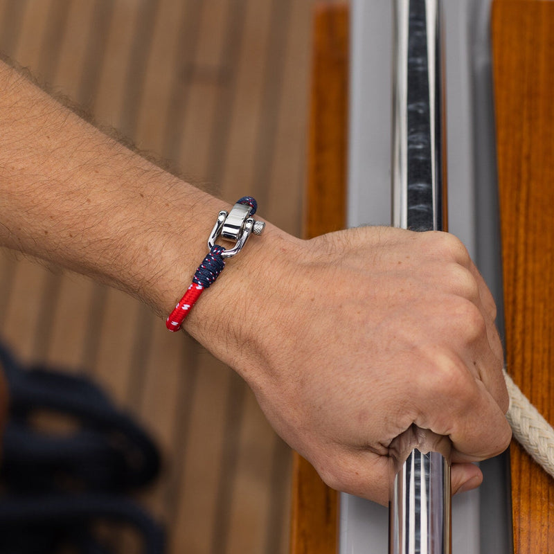 Bracelet cordon bleu et rouge avec mousqueton métallique brillant sur poignet homme.