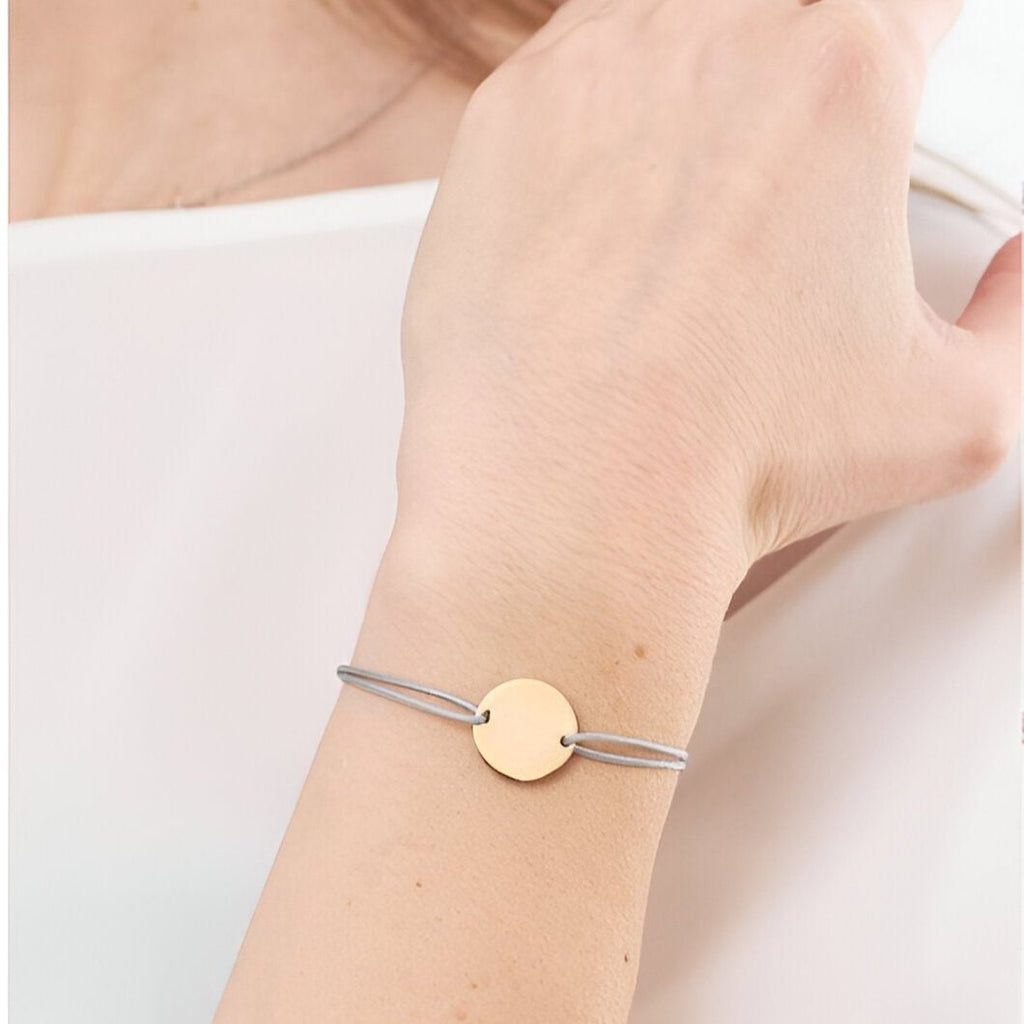 Bracelet cordon gris avec disque lisse en acier inoxydable or rosé sur poignet féminin.