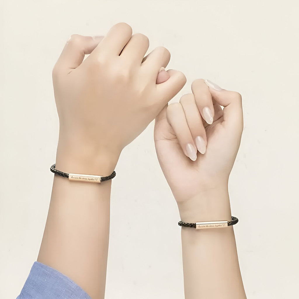 Bracelet cordon noir en cuir avec plaque personnalisable couleur or rose, modèle Grety, porté aux poignets.