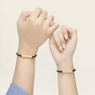 Bracelet cordon noir en cuir avec plaque personnalisable couleur or rose, modèle Grety, porté aux poignets.