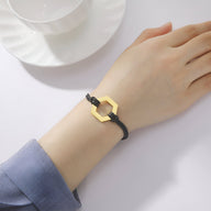 Bracelet cordon noir avec hexagone en acier inoxydable doré, style moderne et épuré.