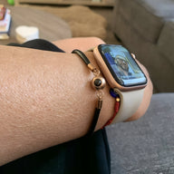 Bracelet photo personnalisé en cuir noir avec détail en acier doré, porté au poignet avec montre connectée blanche.