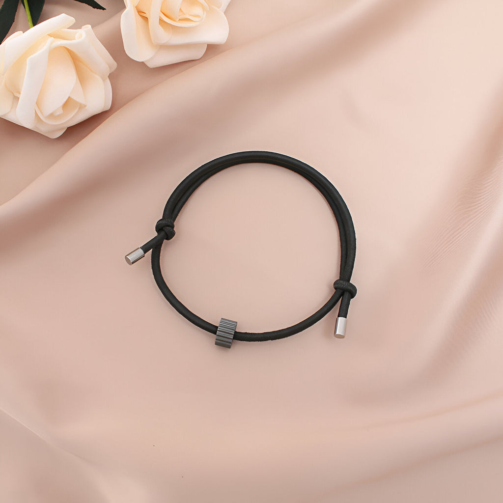 Bracelet cordon noir avec ornement en carbure de tungstène gris et embouts métalliques sur tissu beige.