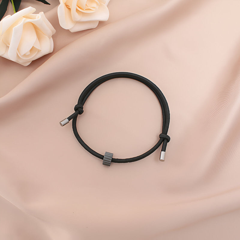 Bracelet cordon noir avec ornement en carbure de tungstène gris et embouts métalliques sur tissu beige.