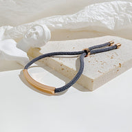 Bracelet cordon noir avec détail gourmette doré en acier inoxydable sur fond clair.