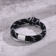 Bracelet cordon noir à rayures blanches avec fermoir métallique argenté et nœud décoratif.