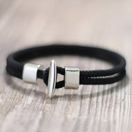 Bracelet cordon noir pour homme avec fermoir argenté en boucle et bouchon cylindrique.