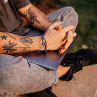 Bracelet cordon gris avec mousqueton argenté sur poignet tatoué, style décontracté homme.