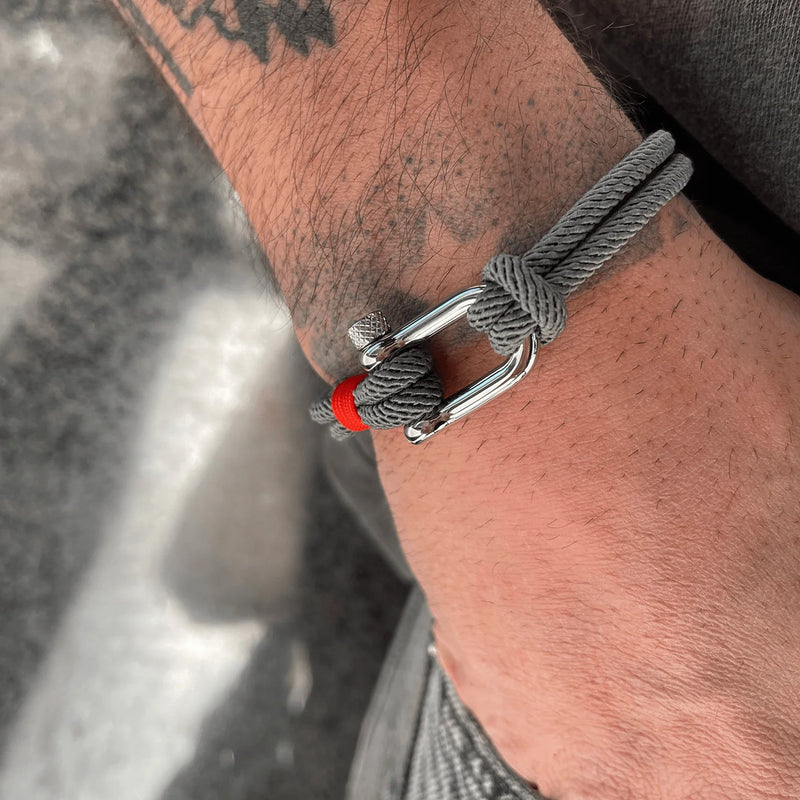 Bracelet cordon gris avec mousqueton argenté et détail rouge, style masculin moderne.