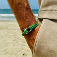 Bracelet cordon vert avec mousqueton argenté sur poignet d'homme, style décontracté plage.