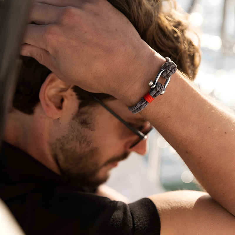 Bracelet cordon gris avec mousqueton argenté et détail rouge, style masculin moderne.