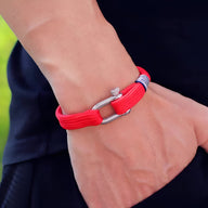Bracelet cordon rouge avec mousqueton argenté, style Mano, porté au poignet homme.