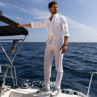 Bracelet cordon gris avec mousqueton arrondi porté par homme en tenue blanche sur voilier, mer en arrière-plan.