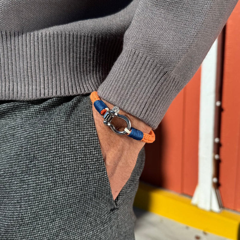 Bracelet cordon orange et bleu avec mousqueton arrondi en métal porté au poignet.