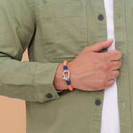 Bracelet cordon orange avec mousqueton arrondi en métal porté sur poignet masculin.