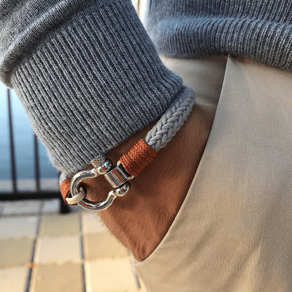 Bracelet cordon gris et orange avec mousqueton arrondi en métal porté au poignet.