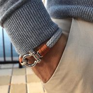 Bracelet cordon gris et orange avec mousqueton arrondi en métal porté au poignet.