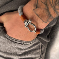 Bracelet cordon gris et orange avec mousqueton arrondi en métal argenté sur poignet tatoué.