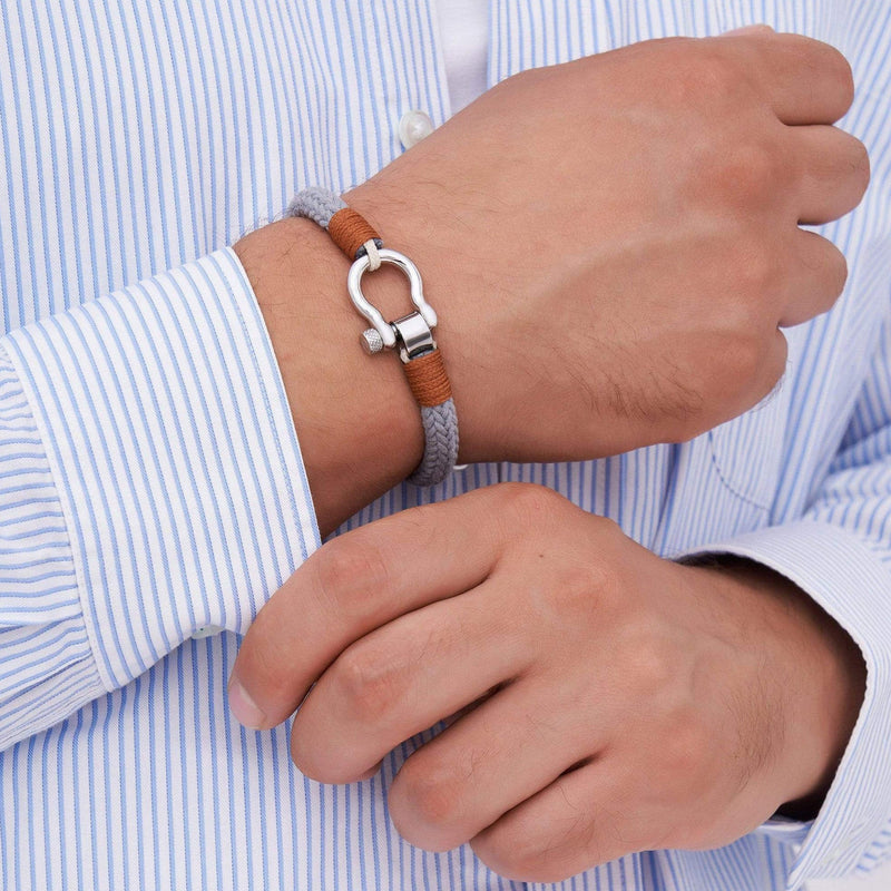 Bracelet cordon gris avec mousqueton métallique arrondi et détails en cuir marron porté au poignet.