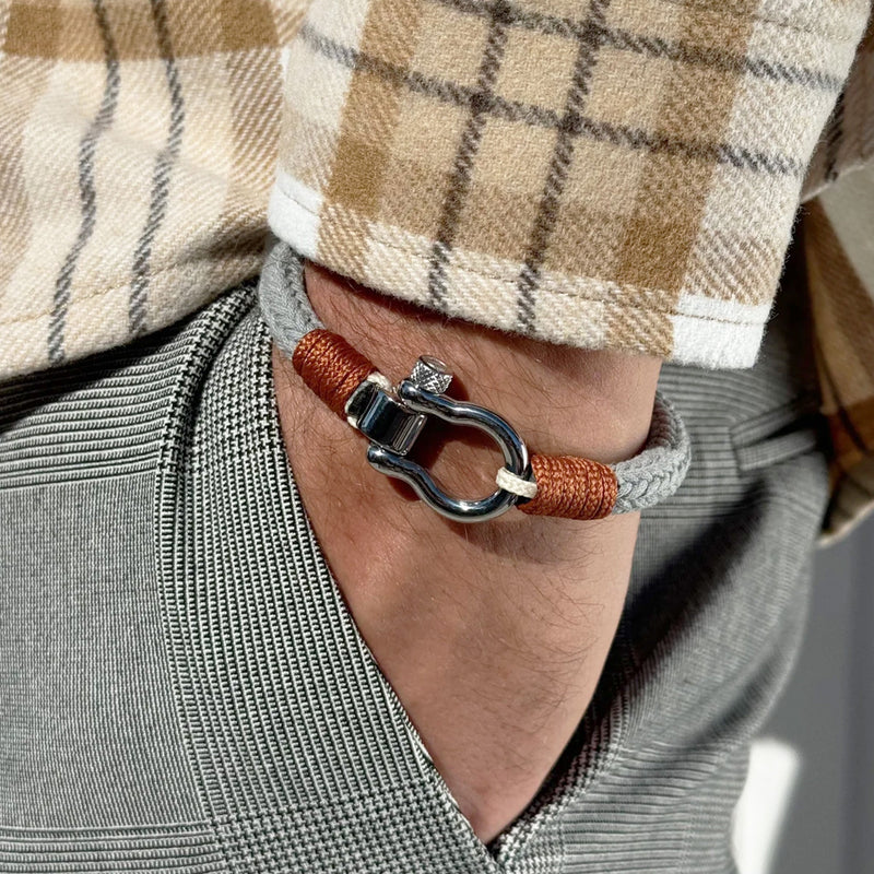 Bracelet cordon gris et orange avec mousqueton arrondi en métal argenté porté au poignet.