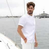 Bracelet cordon rouge pour homme avec mousqueton et détails argentés porté au poignet sur fond de bord de mer.