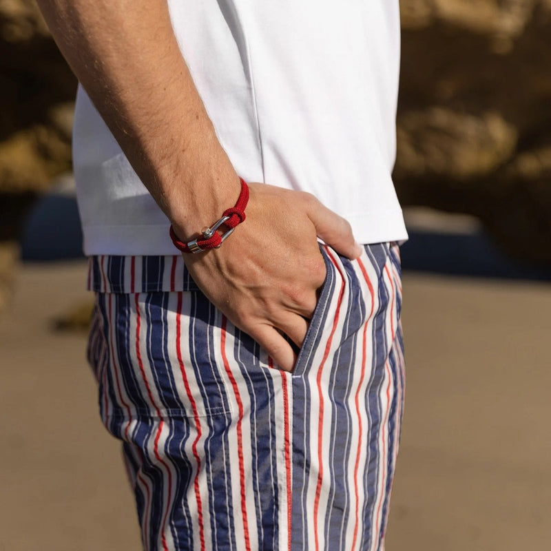 Bracelet cordon rouge pour homme avec mousqueton et détails argentés porté au poignet.