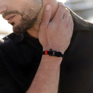 Bracelet cordon noir avec mousqueton noir et détail rouge porté au poignet d’un homme.