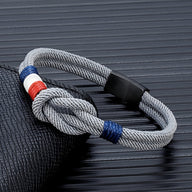 Bracelet cordon gris clair avec nœud et drapeau français, fermoir noir mat.