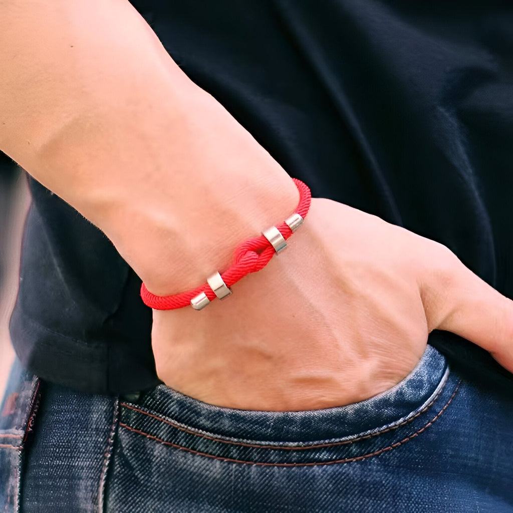 Bracelet cordon rouge avec perles argentées, style simple et masculin, porté au poignet.