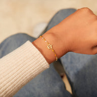 Bracelet fin en or avec pendentif couronne stylisée, porté au poignet féminin.