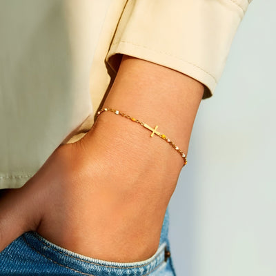 Bracelet fin en or avec croix chrétienne délicate sur poignet féminin, style minimaliste.