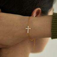 Bracelet doré fin avec croix chrétienne scintillante en petites pierres sur poignet féminin.
