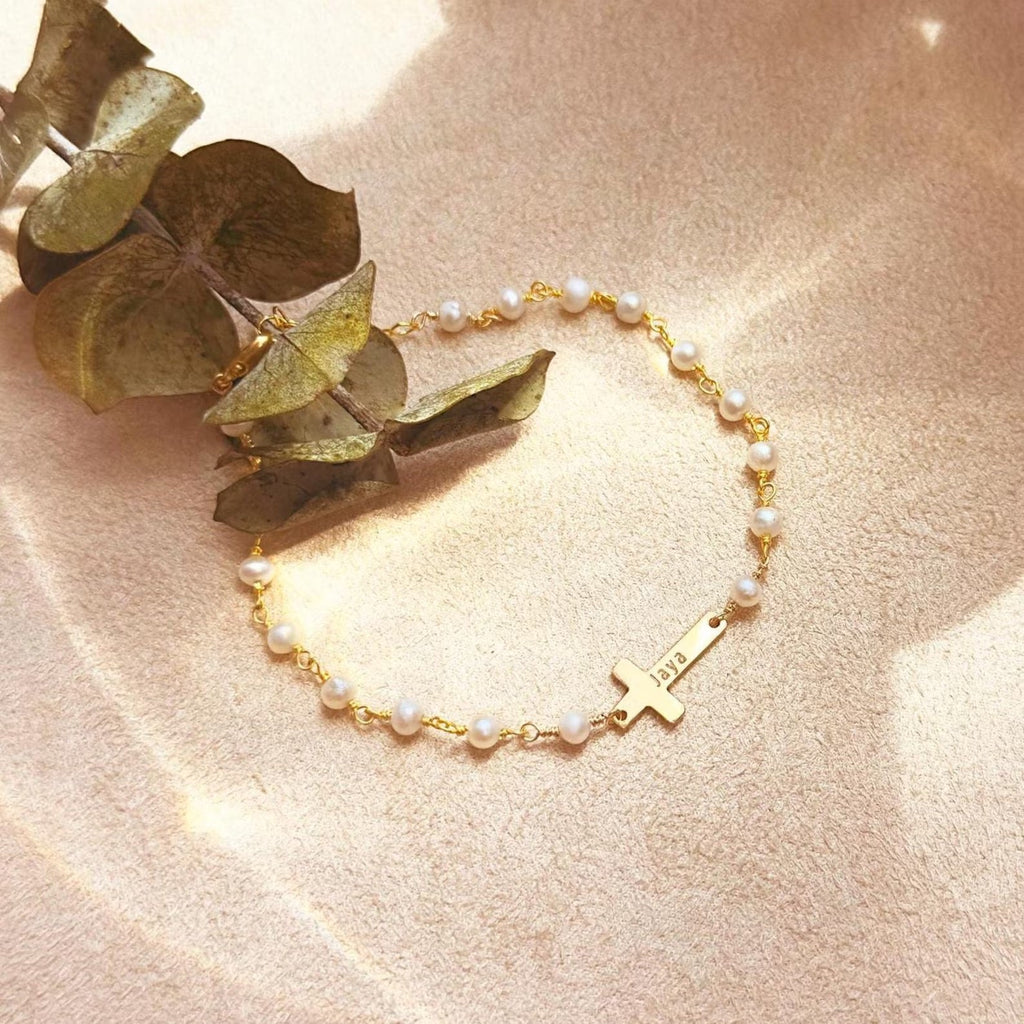 Bracelet doré avec perles d’eau douce fines et croix en acier inoxydable, style délicat et féminin.