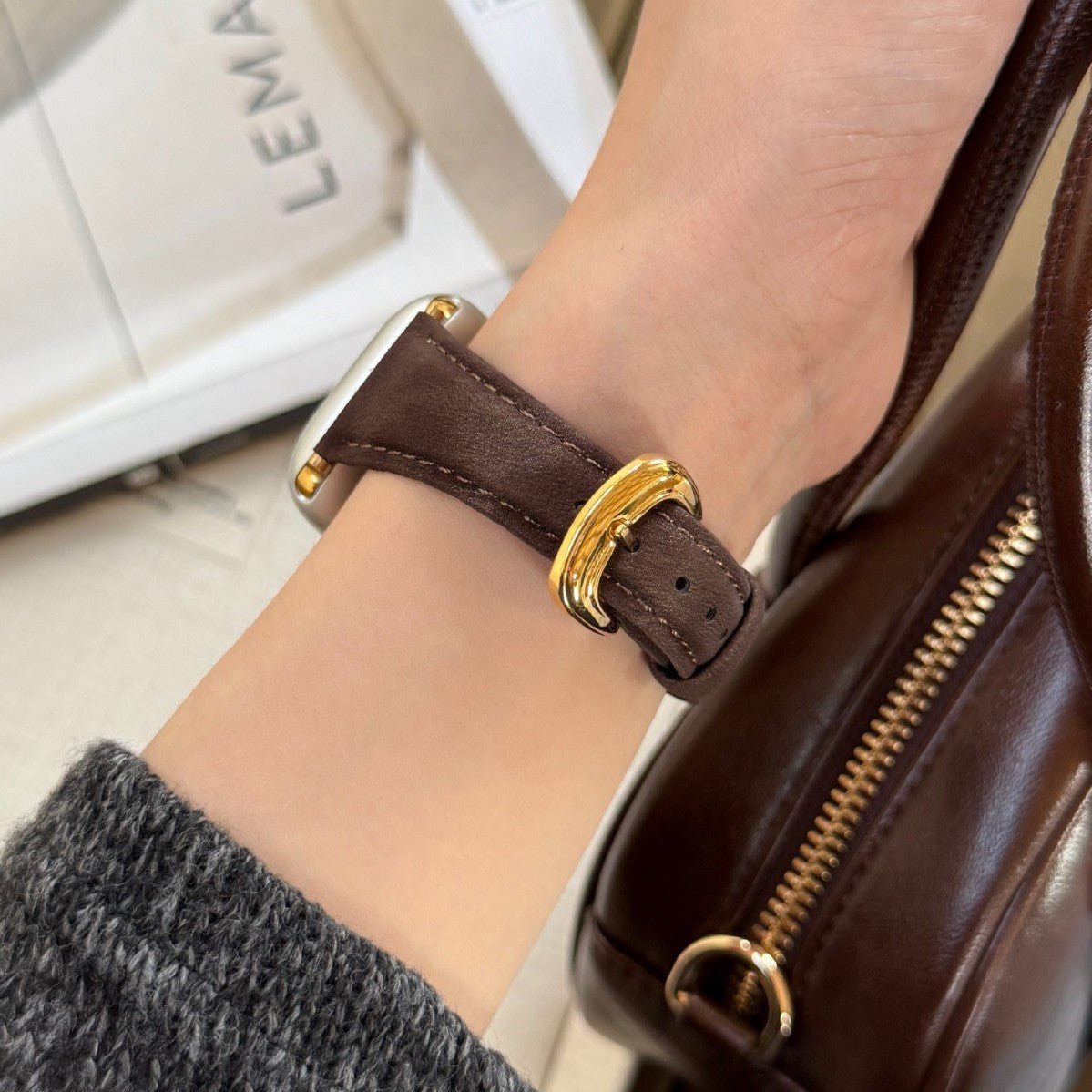 Bracelet en cuir marron foncé avec boucle dorée, ajusté au poignet pour Apple Watch.