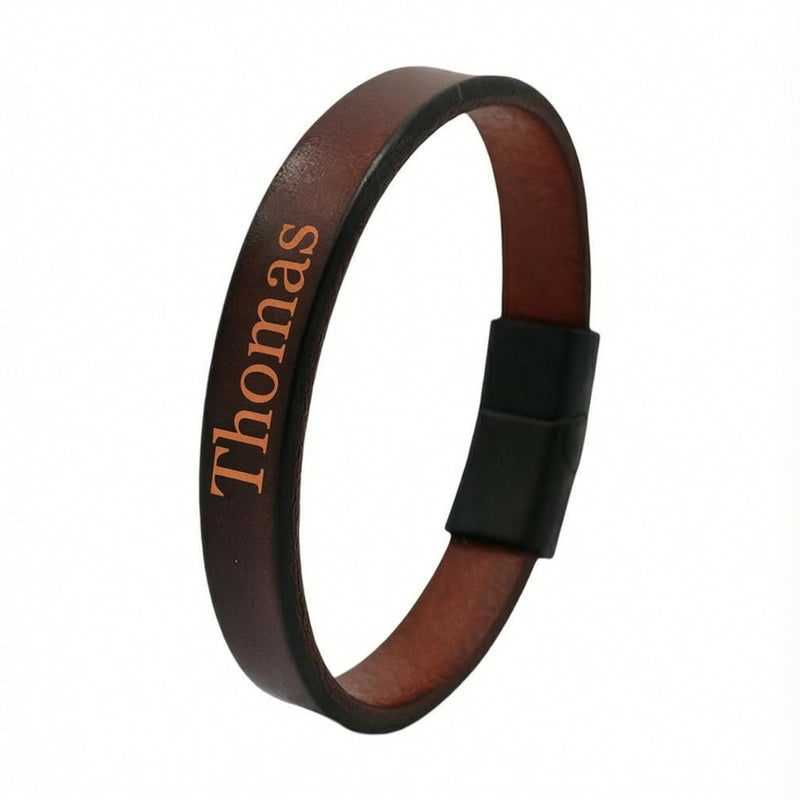Bracelet en cuir marron foncé avec gravure personnalisée "Thomas" en lettres orange, fermoir aimanté noir mat.