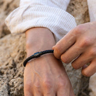 Bracelet homme en cuir noir tressé avec fermoir magnétique métallique gravé, style élégant et moderne.