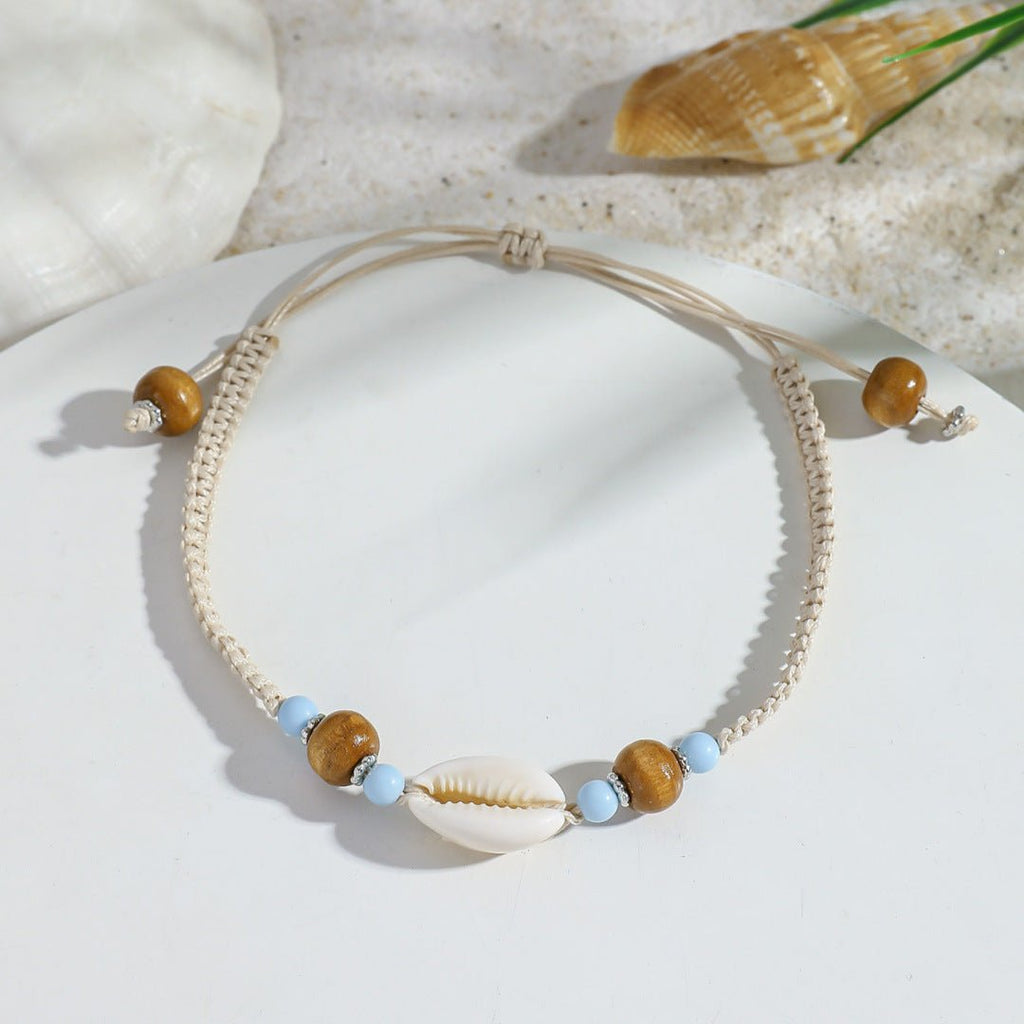 Bracelet de cheville beige en corde avec coquillage central blanc et perles marron et bleues.