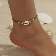 Bracelet de cheville en corde marron avec coquillage blanc et perles bleues sur peau bronzée.