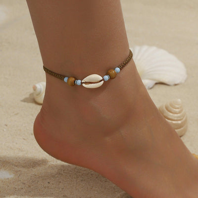 Bracelet de cheville en corde marron avec coquillage blanc et perles bleues sur peau bronzée.