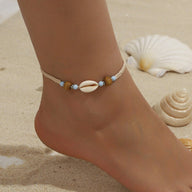 Bracelet de cheville beige en corde avec coquillage et perles colorées sur pied féminin.