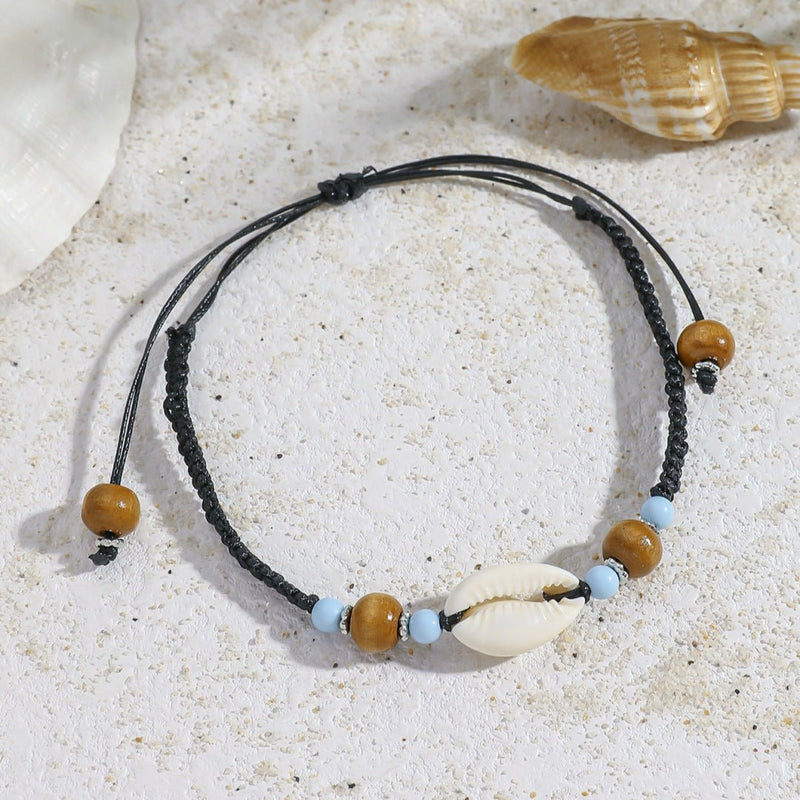 Bracelet de cheville noir en corde avec coquillage blanc et perles en bois clair et bleu ciel.