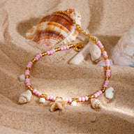 Bracelet de cheville rose avec perles, coquillages et étoile de mer en résine sur sable.