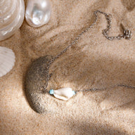 Bracelet de cheville double en acier inoxydable argenté avec coquillage et perle turquoise sur sable.