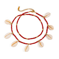 Bracelet de cheville double tour rouge avec perles en résine et coquillages blancs et détails dorés.