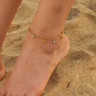 Bracelet de cheville double rang en acier doré avec petites turquoises et breloques fines.